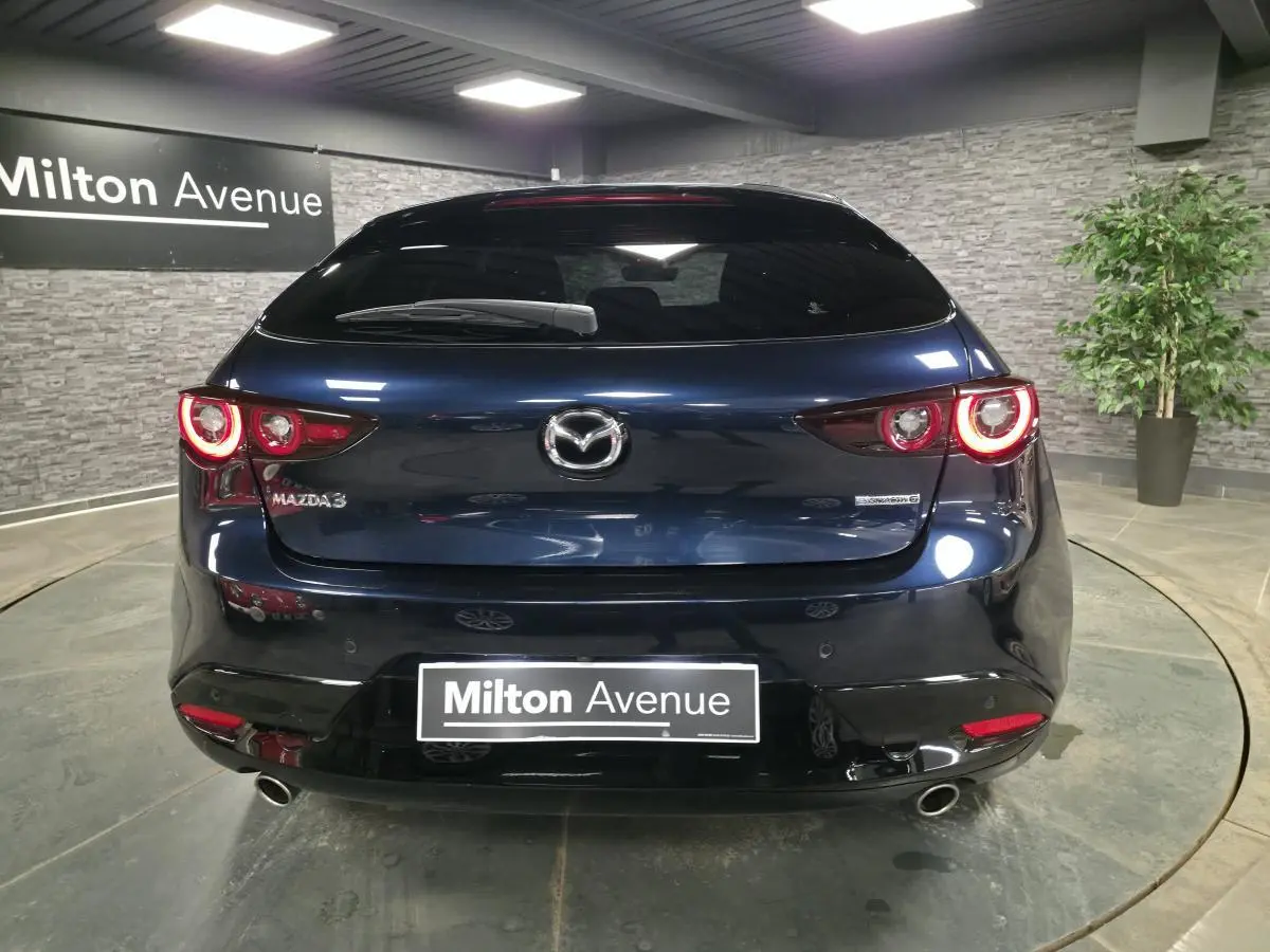 Vue arrière d'une Mazda3 bleu métallisé 2024 avec feux LED circulaires allumés dans un showroom.