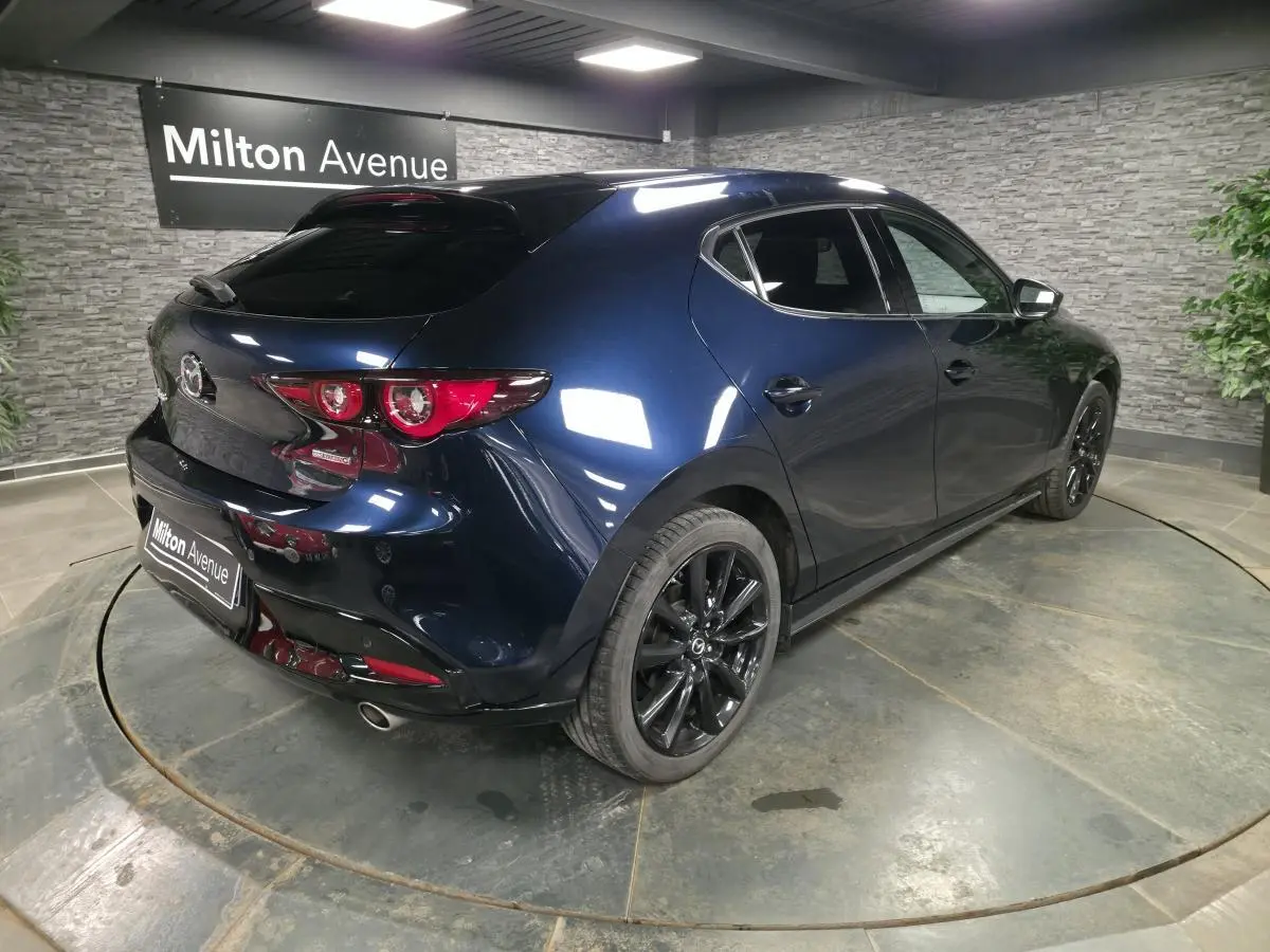 Vue 3/4 arrière droite d'une Mazda3 2024 bleu métallisé avec jantes alliage noires et becquet de toit.