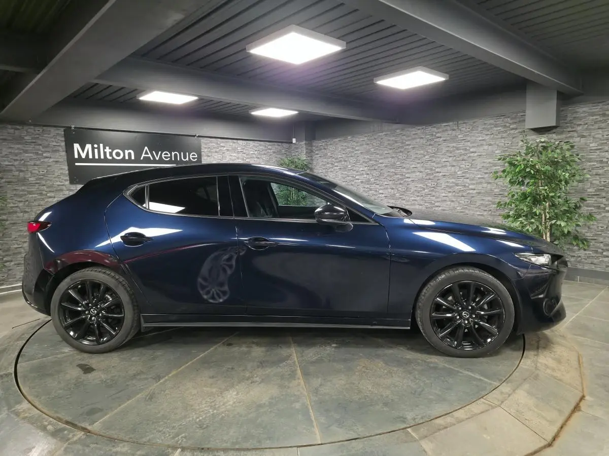 Vue latérale droite d'une Mazda3 2024 bleu métallisé avec jantes alliage noires dans un showroom.