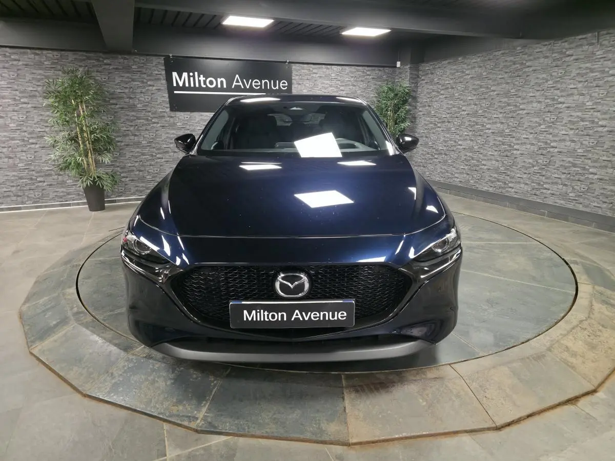 Vue frontale d'une Mazda3 2024 bleu métallisé avec calandre noire et éclairage LED dans un showroom.
