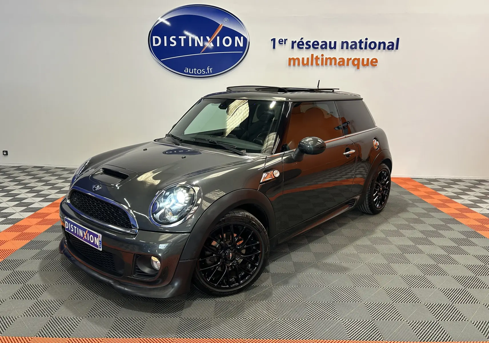 Vue 3/4 avant droite d'une MINI Cooper gris foncé avec jantes noires et toit ouvrant en studio showroom.