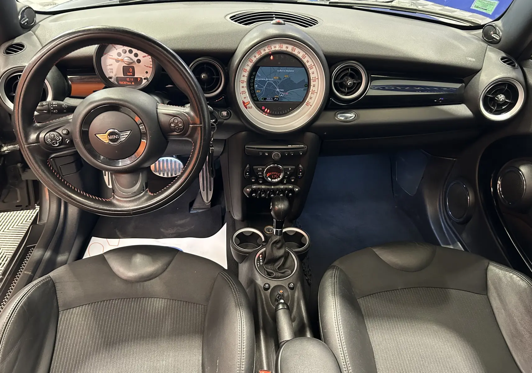 Intérieur noir de MINI Cooper 2011 vu de face, avec tableau de bord rond central affichant un GPS et volant cuir multifonction.