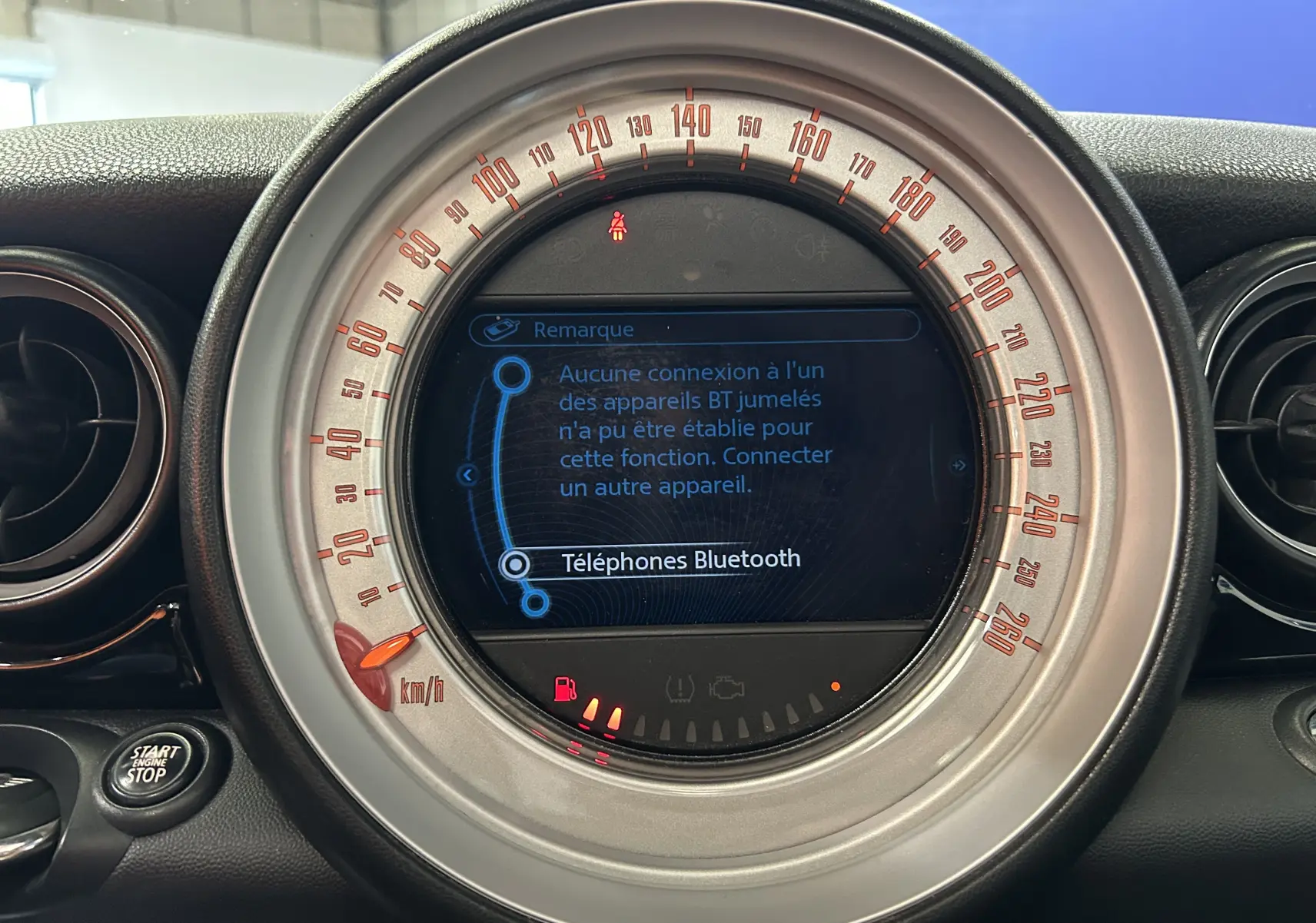 Gros plan sur le compteur central de la MINI Cooper gris, affichant l'écran Bluetooth et le bouton Start/Stop.