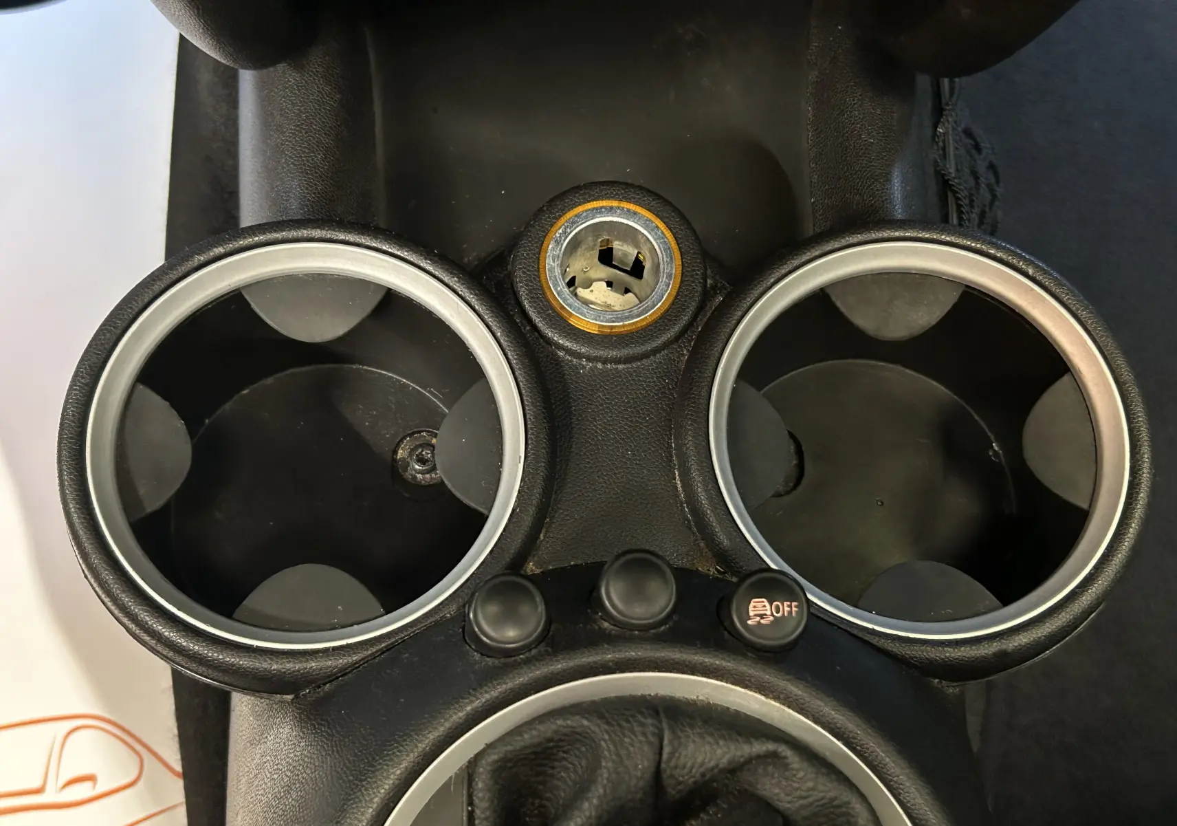 Gros plan sur la console centrale noire de la MINI Cooper 2011, montrant les porte-gobelets et un bouton de désactivation ESP.