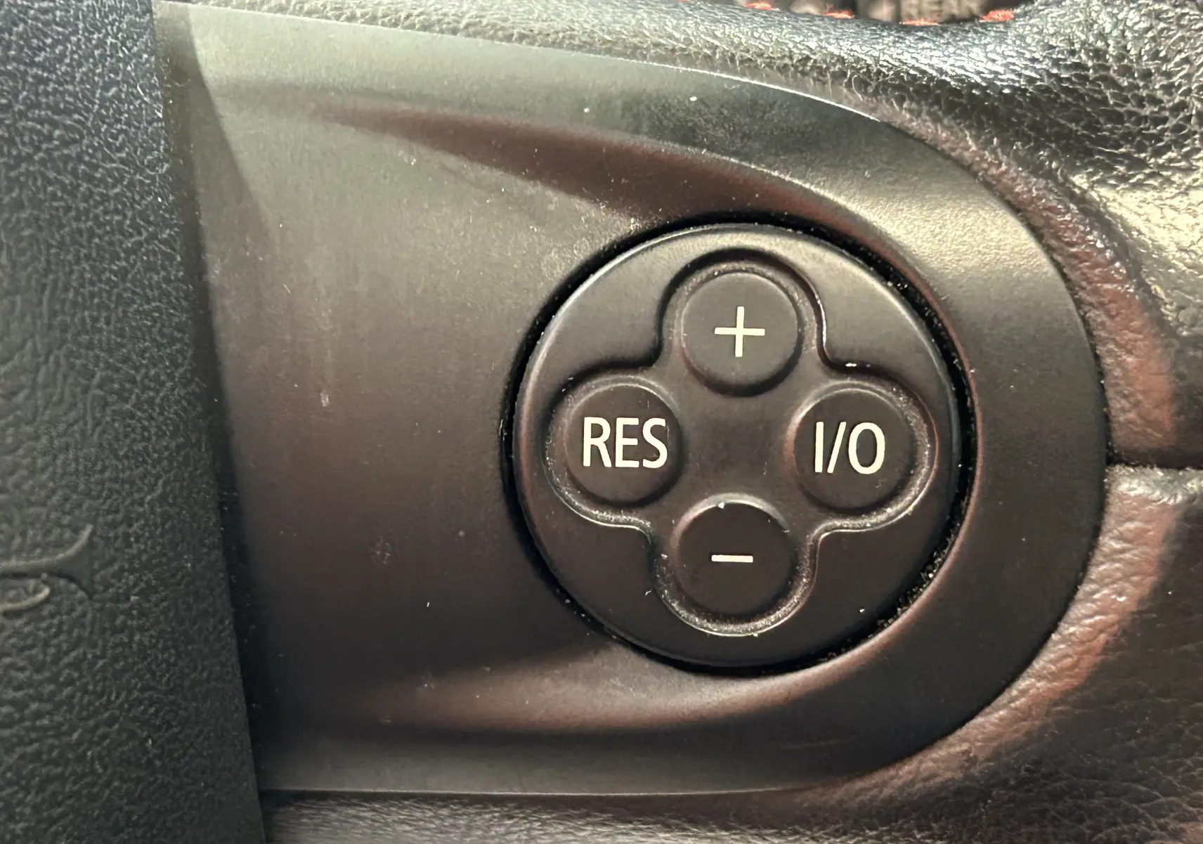Gros plan sur les boutons de commande du régulateur de vitesse sur le volant noir d'une MINI Cooper gris 2011.