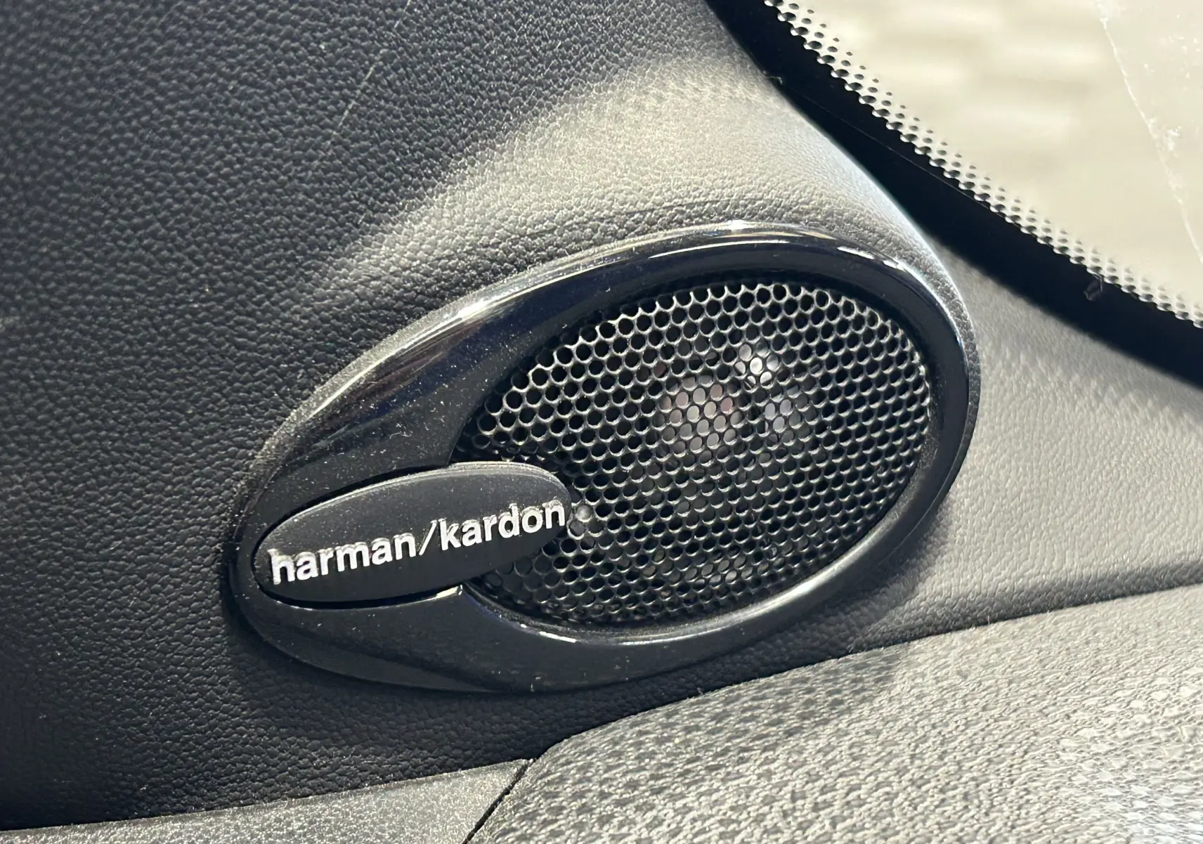 Gros plan sur l'enceinte audio Harman/Kardon intégrée dans l'habitacle noir d'une MINI Cooper gris 2011.