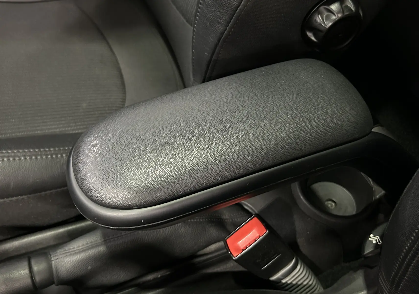 Détail de l'accoudoir central noir et de la ceinture de sécurité rouge dans l'habitacle d'une MINI Cooper gris 2011.