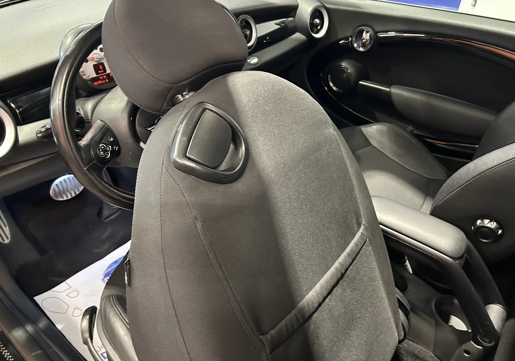 Intérieur de MINI Cooper gris vu côté conducteur, avec siège avant en tissu noir et tableau de bord moderne.