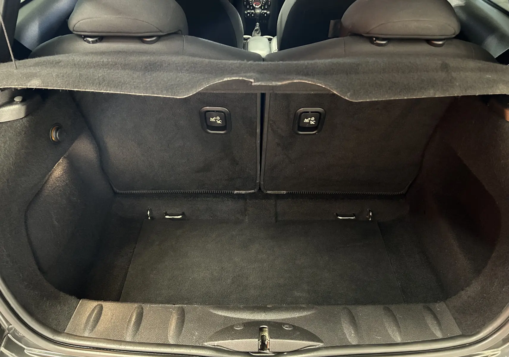 Coffre ouvert vu de l'arrière d'une MINI Cooper gris, montrant l'espace de chargement et les dossiers de sièges rabattables.