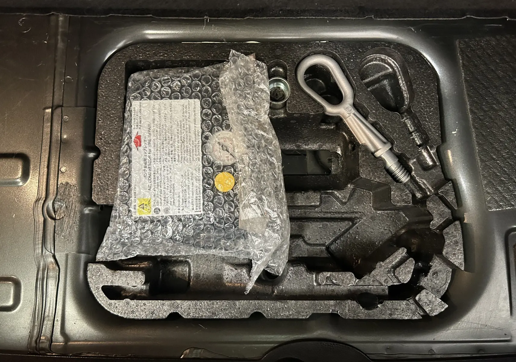 Vue en plongée sur le coffre d'une MINI Cooper gris, montrant le kit de réparation pneu avec outils intégrés.