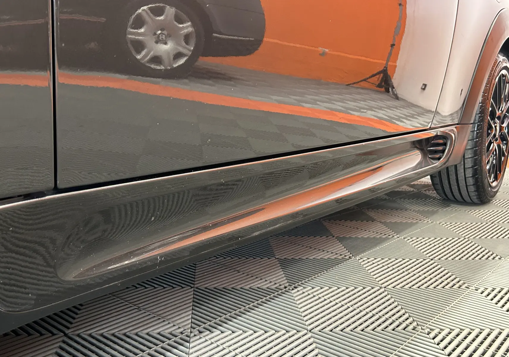 Gros plan sur la partie basse côté droit d’une MINI Cooper gris métallisé avec jante noire et détails aérodynamiques.