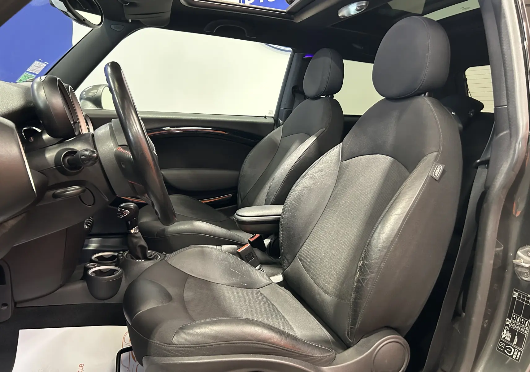 Vue intérieure côté gauche de la MINI Cooper gris, montrant les sièges avant en cuir et le volant avec toit ouvrant partiel.