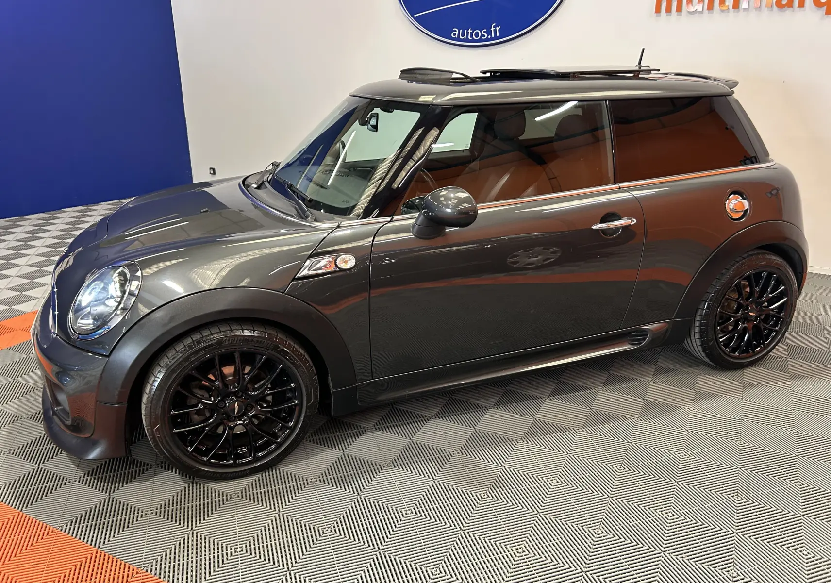 Vue latérale droite d'une MINI Cooper gris métallisé avec jantes noires et toit noir dans un showroom.