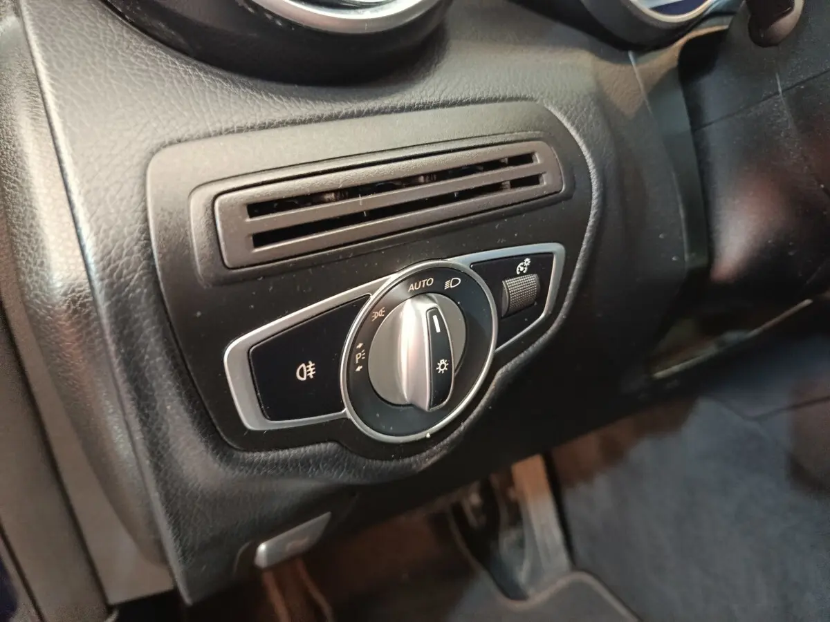 Gros plan sur la commande des phares et la sortie d'air côté gauche du tableau de bord noir d'une Mercedes GLC 300 hybride.