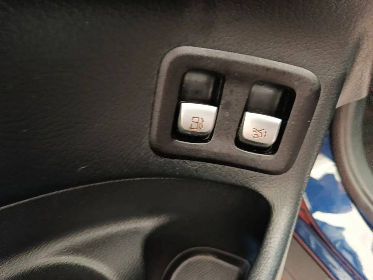 Gros plan sur les boutons d’ouverture de trappe à carburant et coffre dans l’habitacle d’un Mercedes GLC bleu.