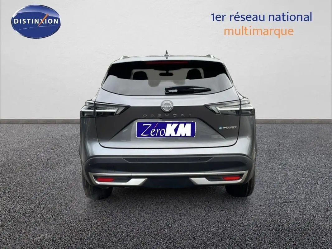Vue arrière d'un Nissan Qashqai gris 2025 avec barres de toit et feux LED, sur fond neutre en extérieur.