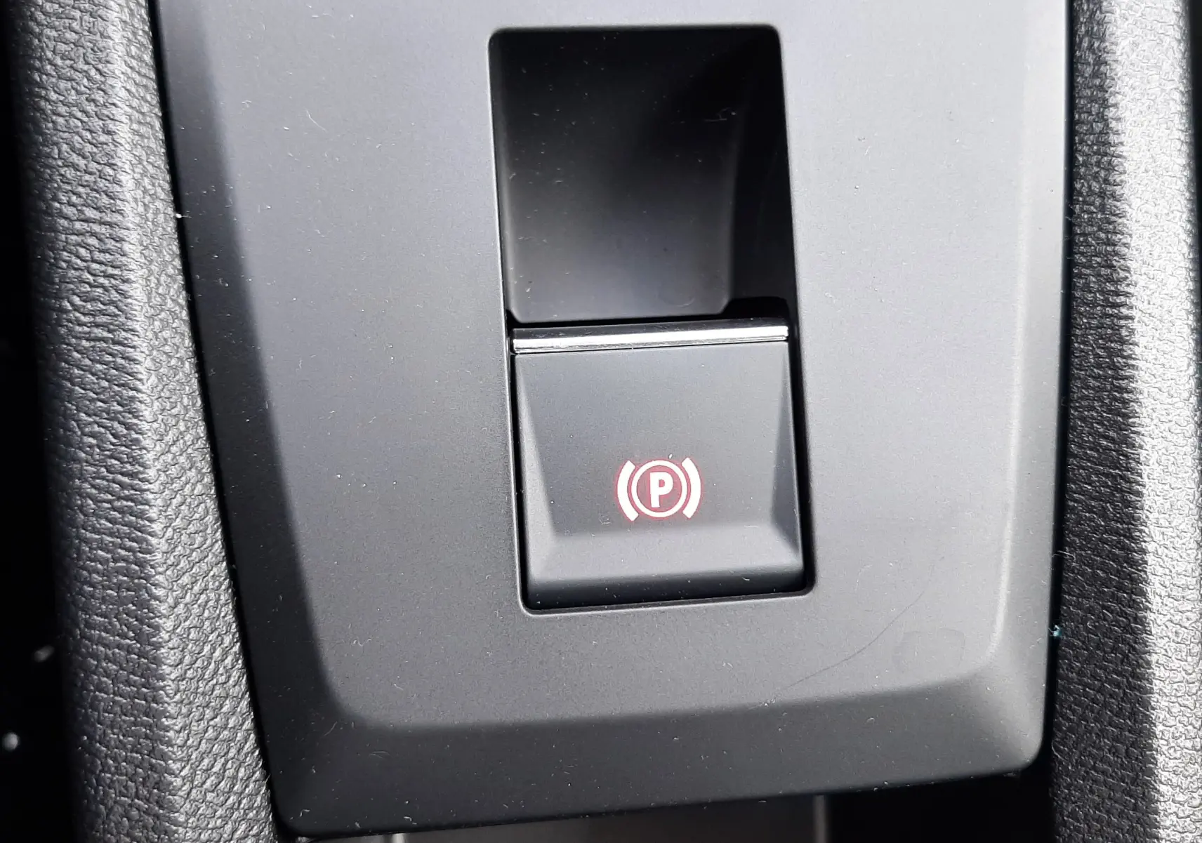 Gros plan sur le bouton de frein à main électronique avec symbole rouge dans l'habitacle du Citroën C3 Aircross blanc banquise.
