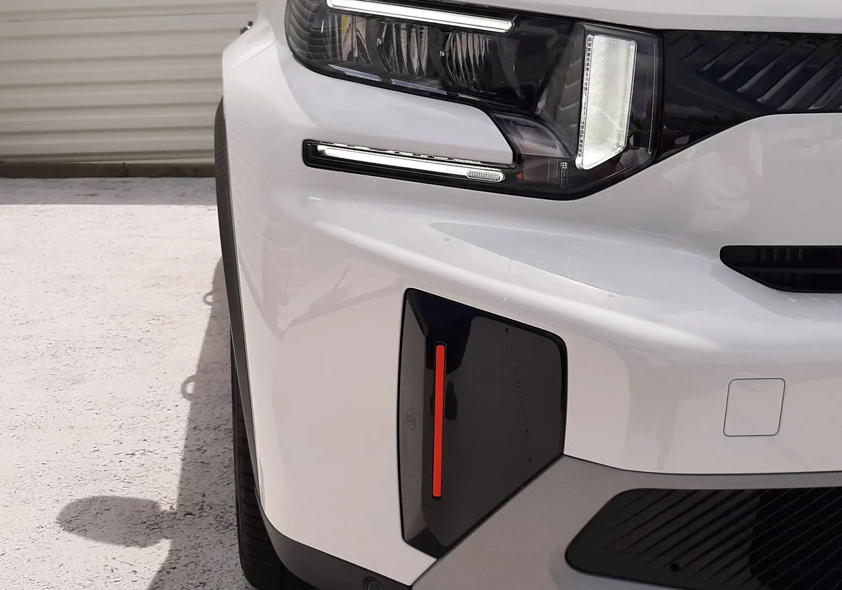 Gros plan sur l'avant gauche du Citroën C3 Aircross blanc banquise avec toit noir, mettant en valeur le phare LED et le détail rouge du pare-chocs.