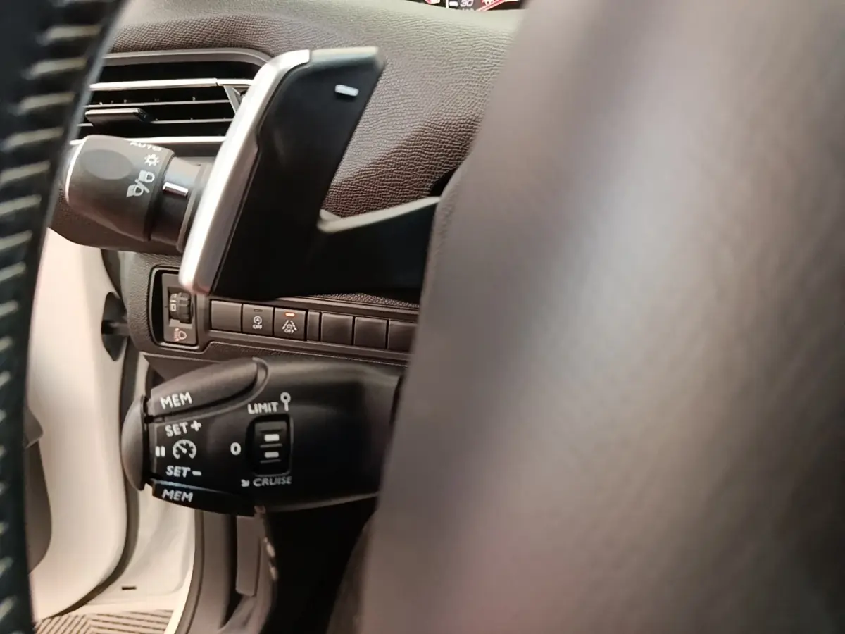 Gros plan sur la commande de régulateur de vitesse à gauche du volant dans l’habitacle blanc du Peugeot 308 2020.