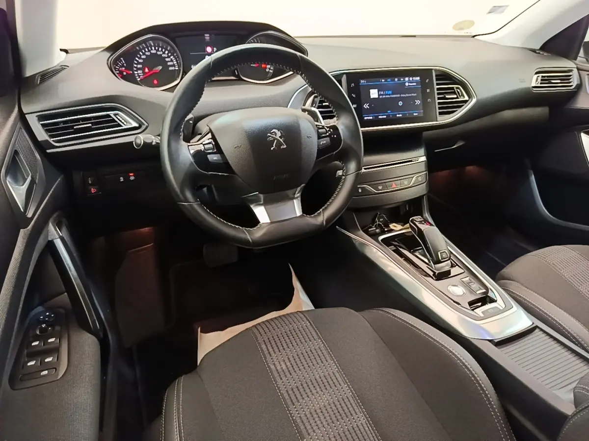 Vue intérieure avant droite de la Peugeot 308 avec volant cuir, écran tactile central et console de boîte automatique.