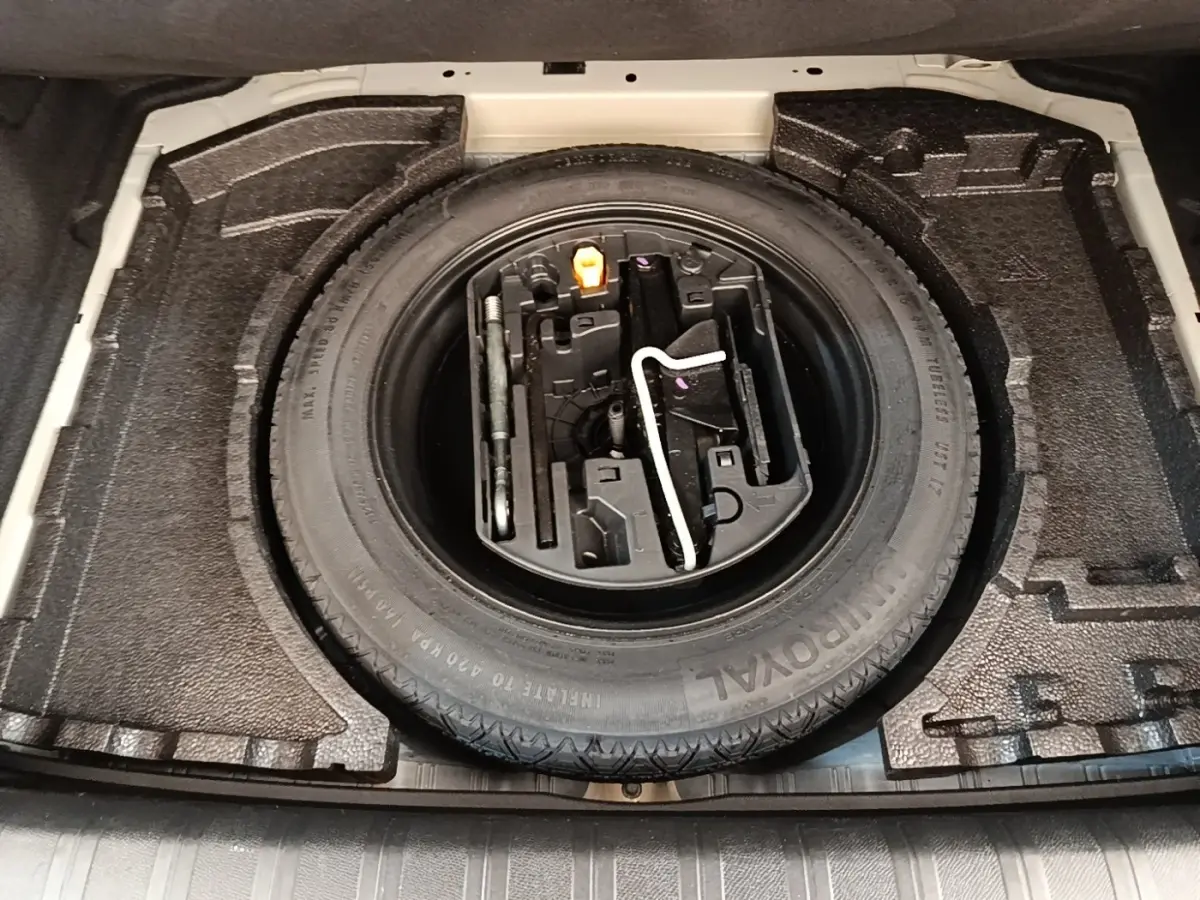 Vue plongeante sur la roue de secours et les outils de bord dans le coffre d'une Peugeot 308 blanche.