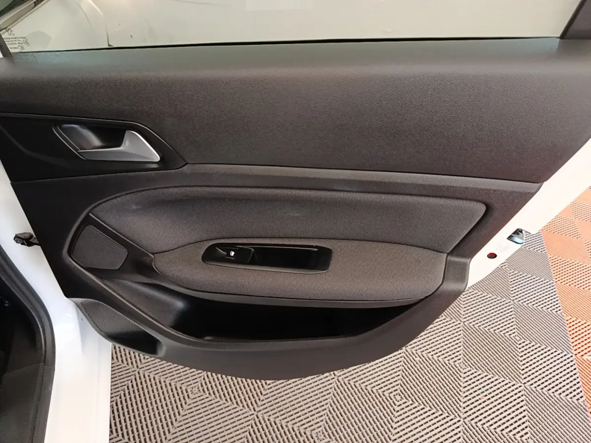 Vue rapprochée de la porte avant gauche blanche d'une Peugeot 308 avec garniture noire et commande de lève-vitre.