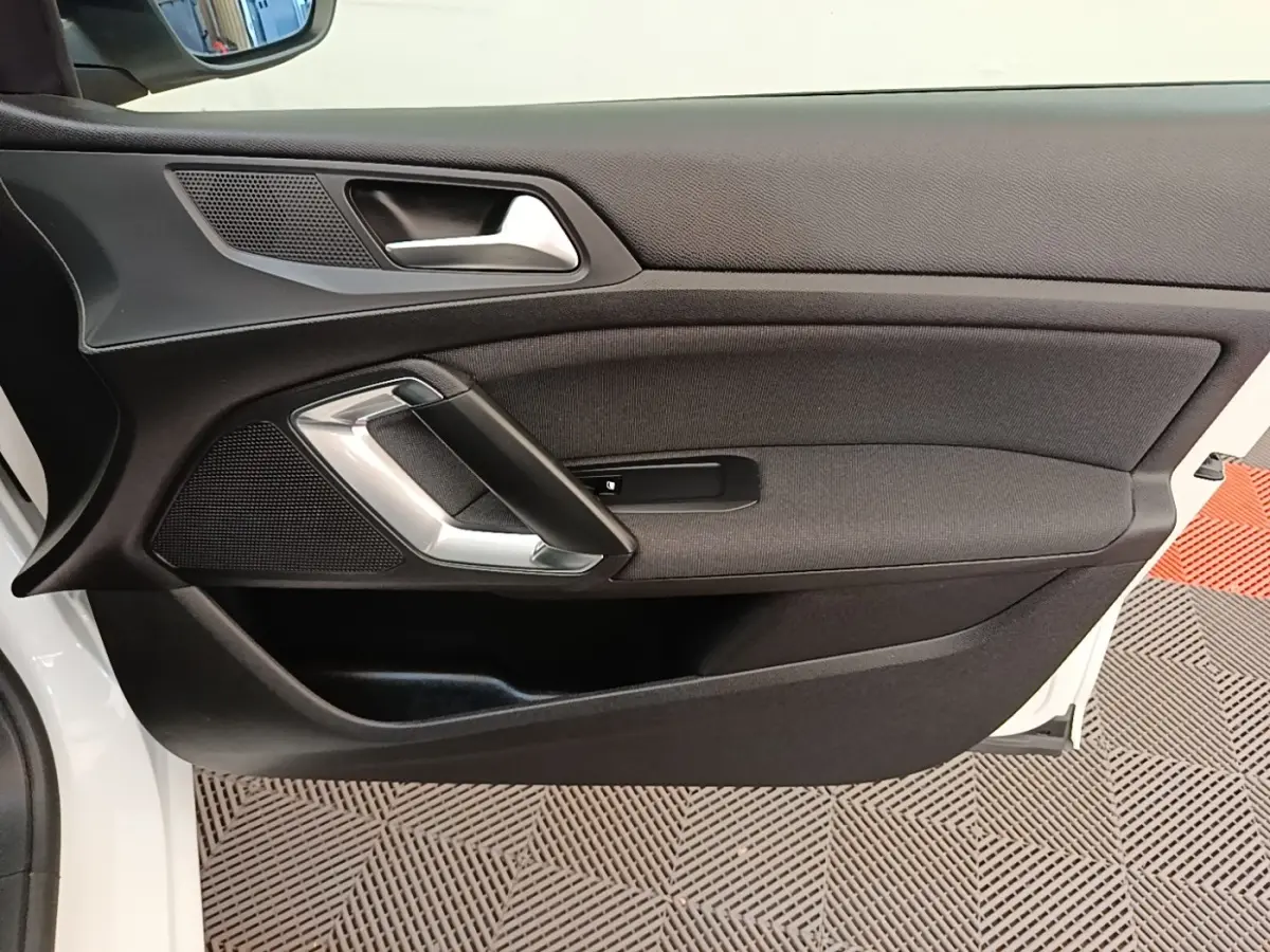 Vue intérieure côté gauche de la porte avant blanche de la Peugeot 308 avec poignée argentée et garniture noire.