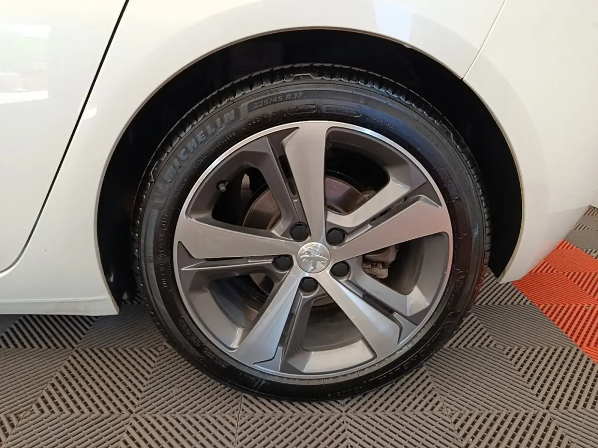 Gros plan sur la roue avant droite d'une Peugeot 308 blanche, jante alliage gris foncé au design moderne.