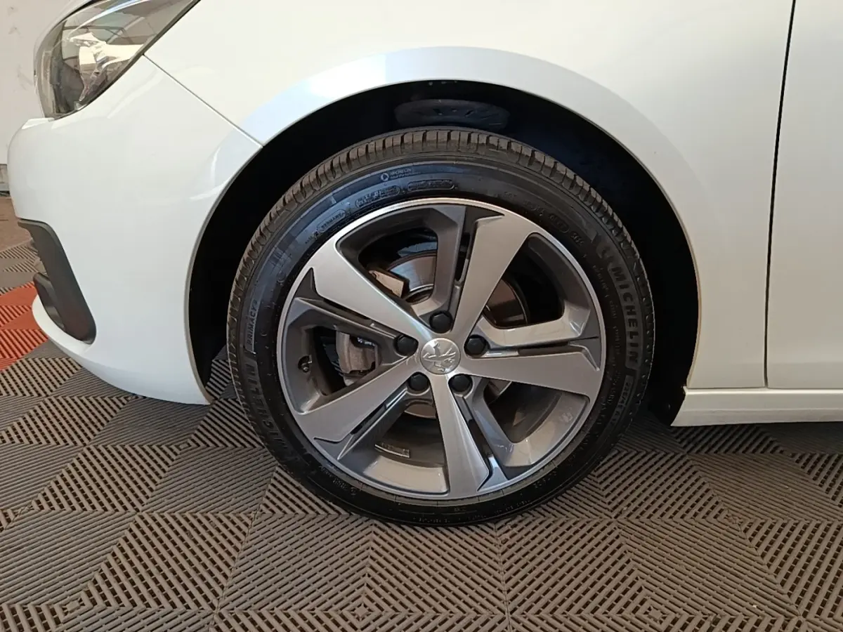 Gros plan sur la roue avant gauche de la Peugeot 308 blanche, mettant en valeur la jante alliage moderne.