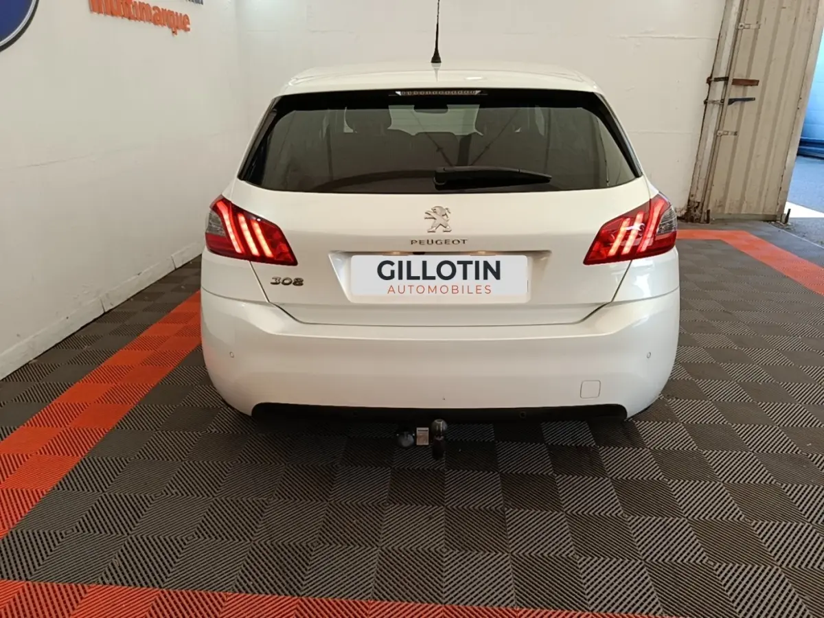 Vue arrière d'une Peugeot 308 blanche avec feux arrière allumés et attelage visible en intérieur showroom.