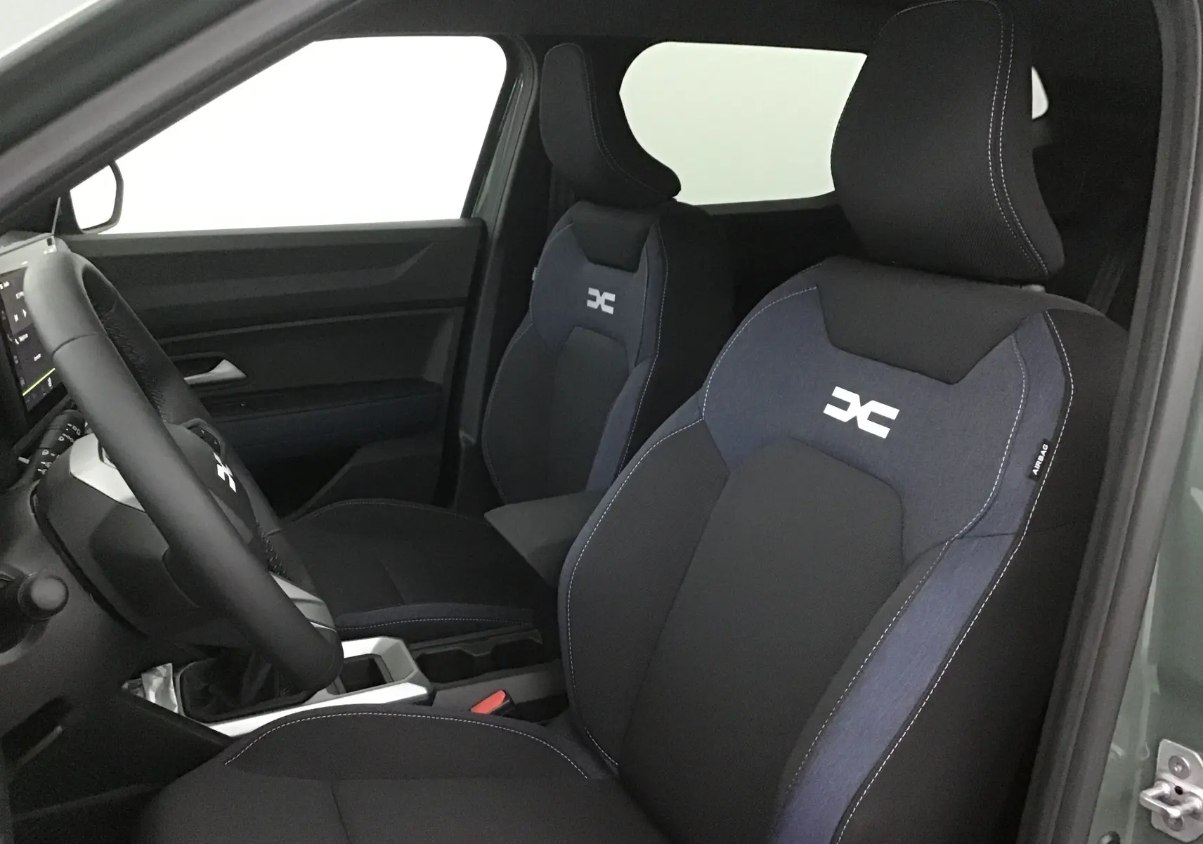Vue intérieure côté conducteur du Dacia Duster 2025 avec sièges noirs et logo blanc sur appuie-tête, ambiance sobre et moderne.