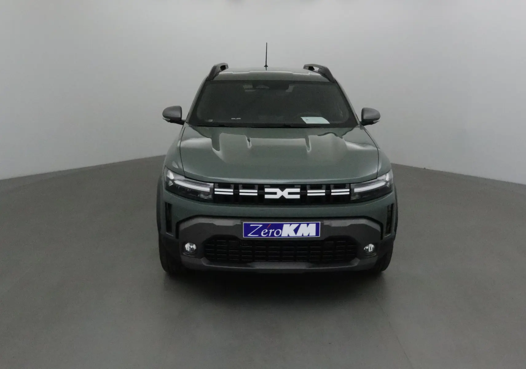 Vue frontale d'un Dacia Duster 2025 kaki lichen avec calandre noire et phares LED fins allumés.