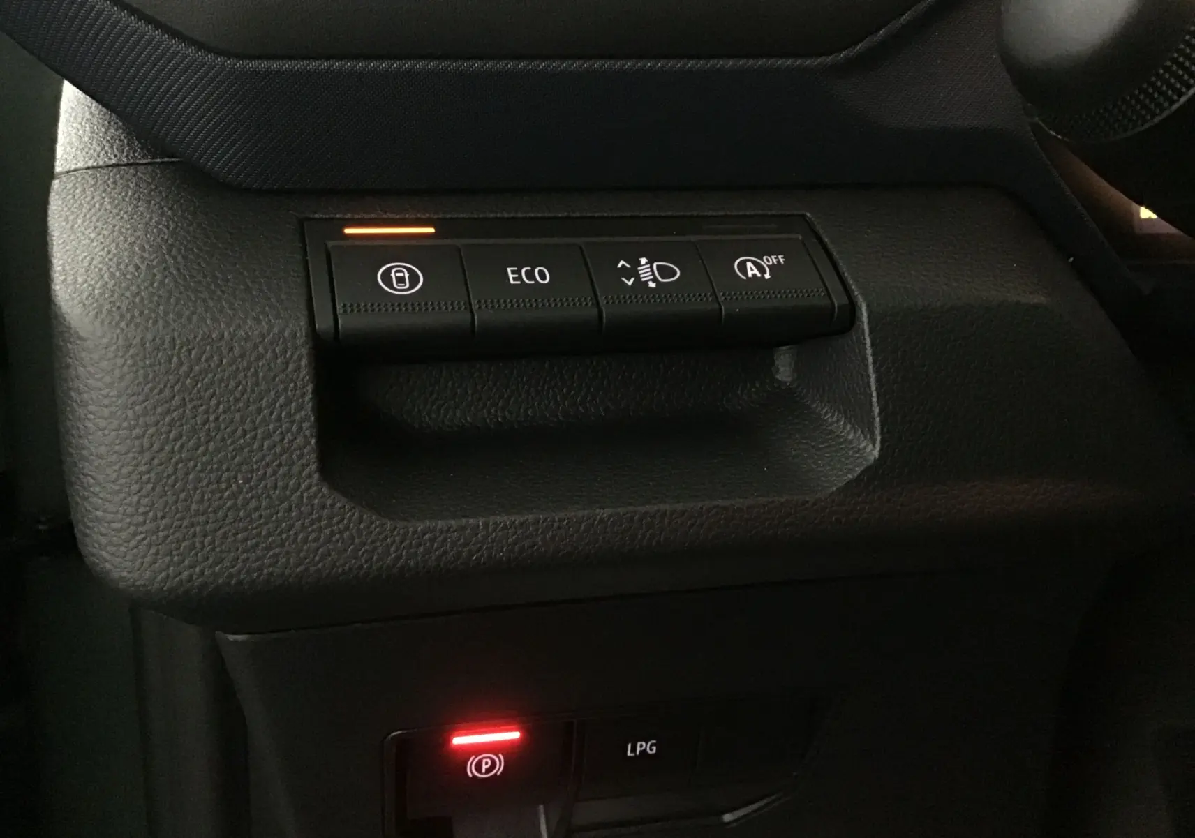 Gros plan sur les commandes noires du tableau de bord du Dacia Duster 2025, avec voyants ECO et frein à main rouges allumés.