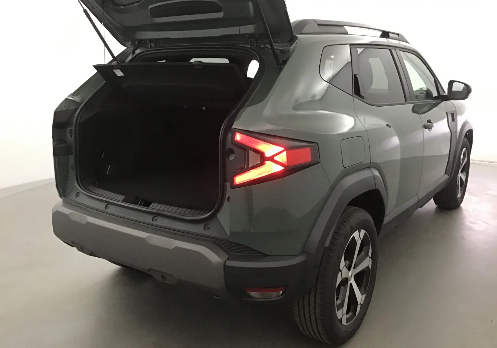 Vue 3/4 arrière droite du Dacia Duster 2025 kaki lichen avec coffre ouvert et feux arrière allumés.