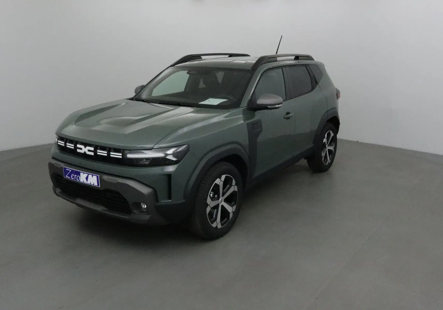 SUV Dacia Duster 2025 kaki lichen en 3/4 avant droit, avec jantes alliage et barres de toit noires.