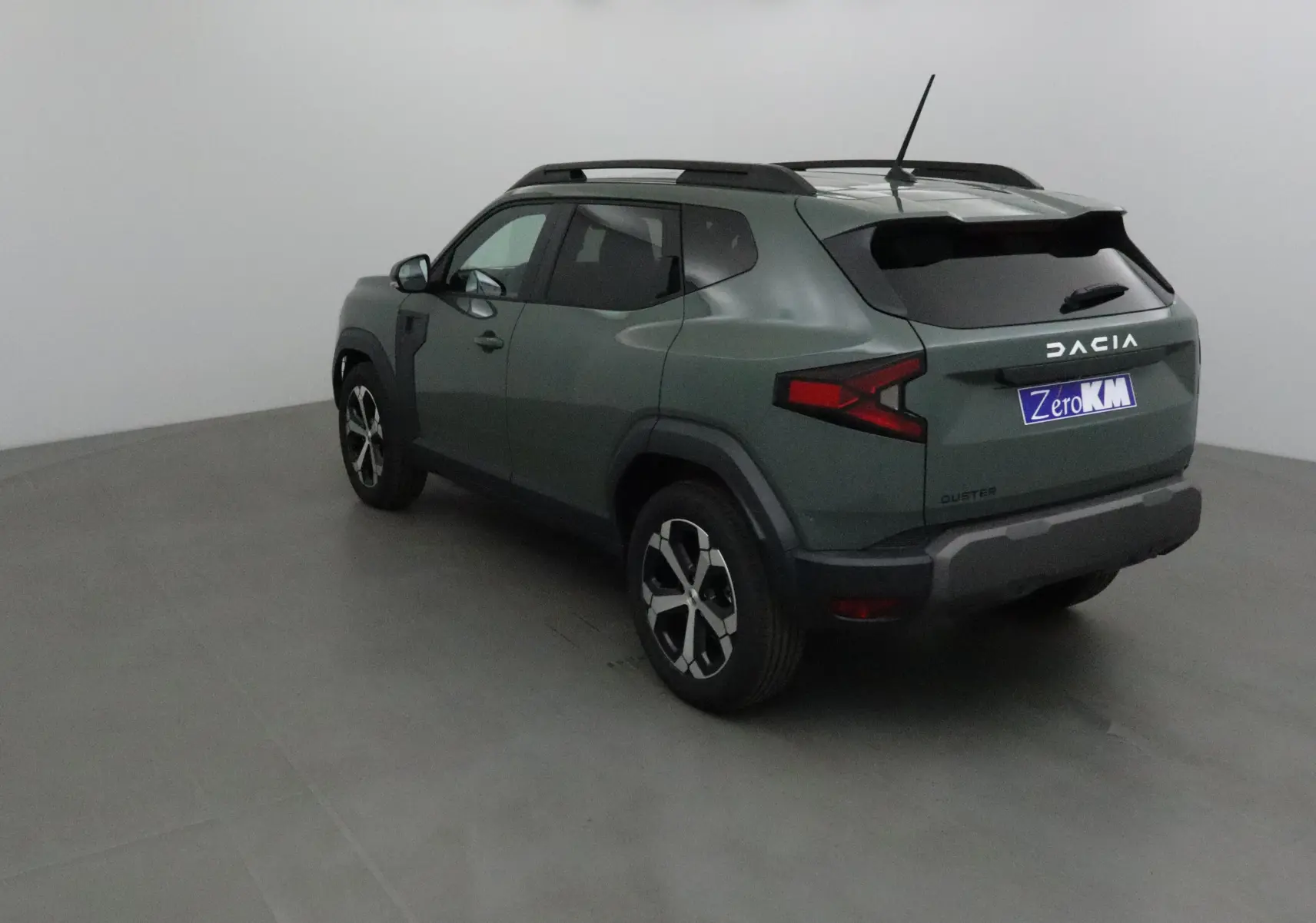 Vue 3/4 arrière gauche d'un Dacia Duster 2025 kaki lichen avec jantes alliage et barres de toit noires.