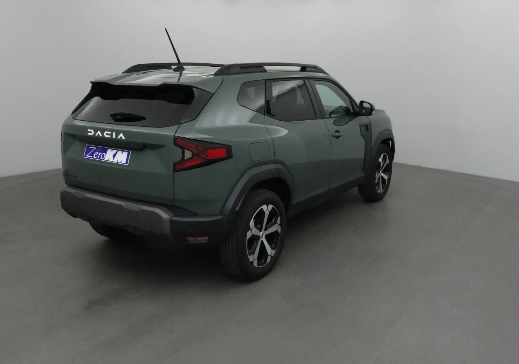 Vue 3/4 arrière droite du Dacia Duster 2025 kaki lichen avec barres de toit et jantes noires et argentées.