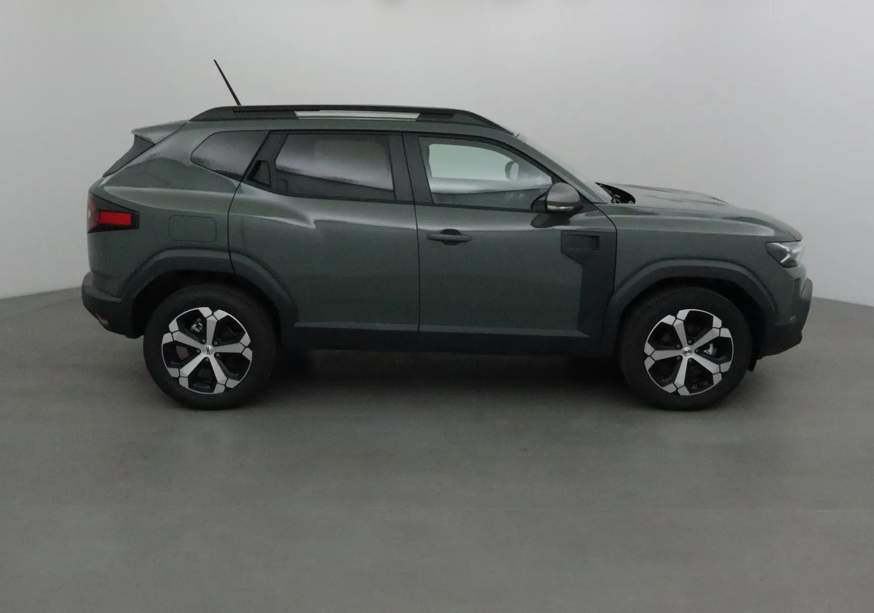 Profil droit du Dacia Duster 2025 en kaki lichen avec jantes alliage et barres de toit noires.
