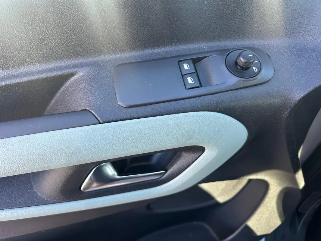 Gros plan sur la commande de lève-vitres et le bouton de réglage des rétroviseurs côté gauche intérieur d’un Citroën Berlingo gris clair.