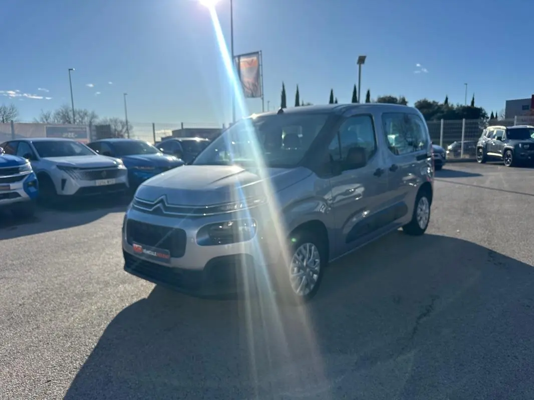 Citroën Berlingo gris clair vue 3/4 avant droit avec protections latérales noires, stationné en extérieur au soleil.