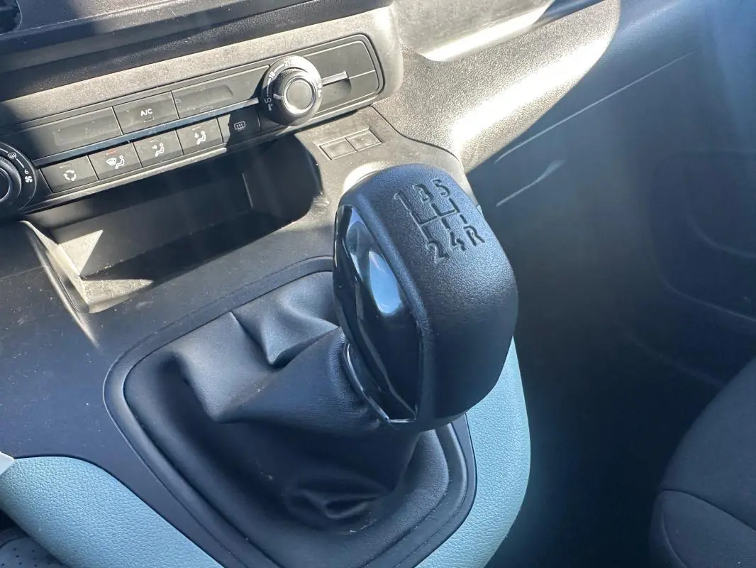Gros plan sur le levier de vitesses manuel noir du Citroën Berlingo gris clair, avec commandes de climatisation en arrière-plan.