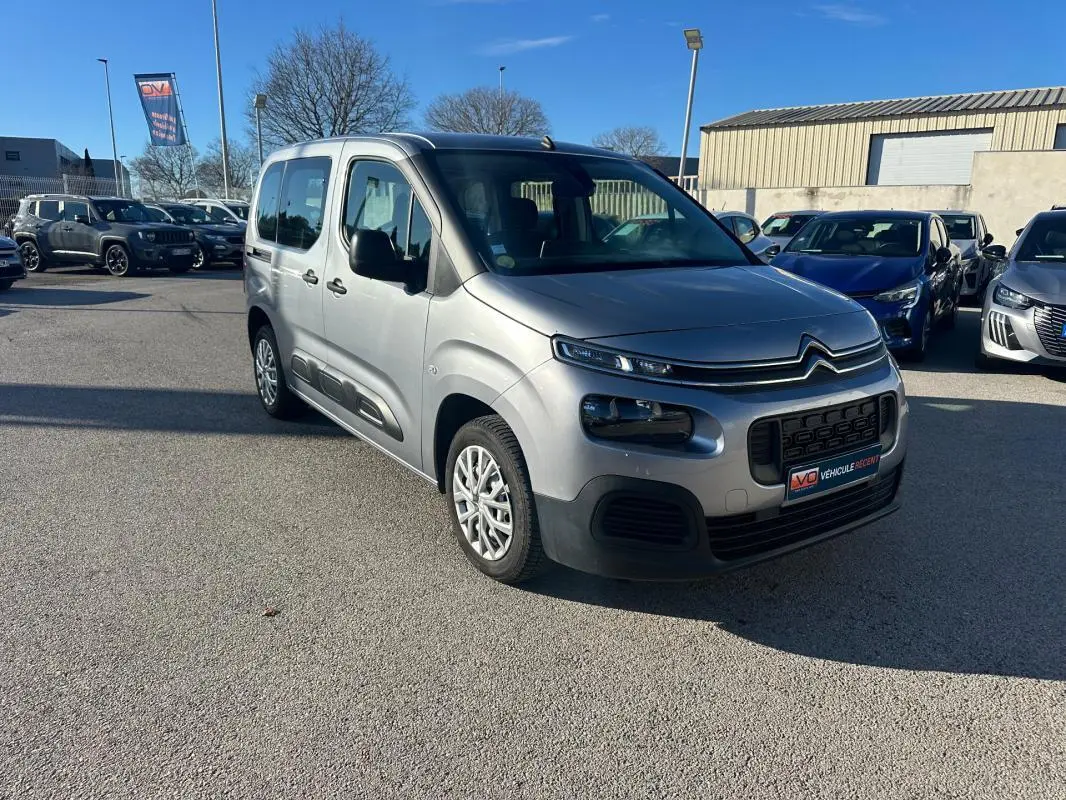 Citroën Berlingo gris clair en 3/4 avant droit, avec protections latérales noires et calandre distinctive.