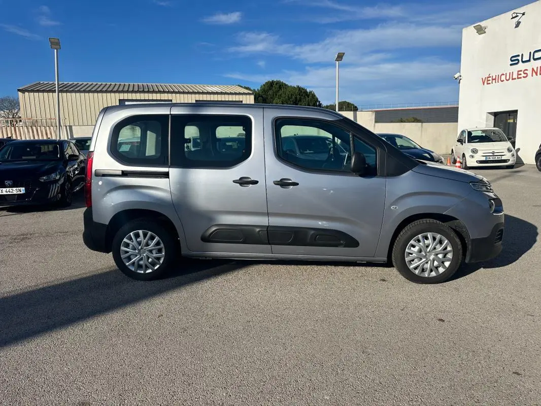 Vue de profil côté droit d'un Citroën Berlingo gris clair 2020 avec protections noires sur les portières, stationné en extérieur.