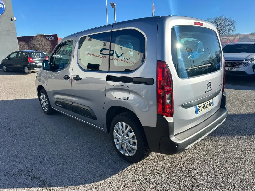 Vue 3/4 arrière droite d'un Citroën Berlingo gris clair 2020 avec vitres teintées et protections noires sur les portes.
