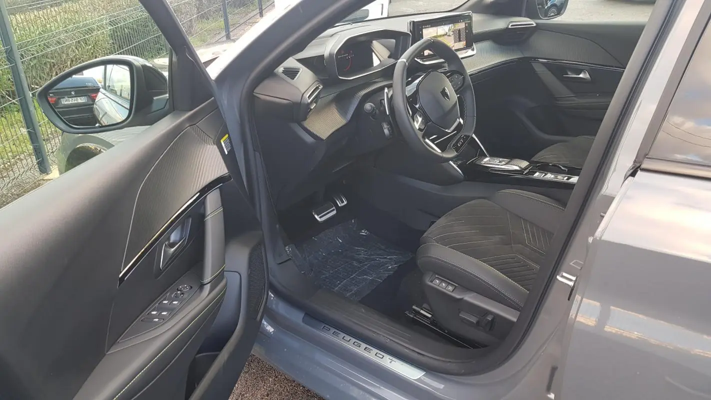 Vue intérieure côté conducteur de la Peugeot 208 gris 2025, mettant en valeur le volant GT et le cockpit numérique.