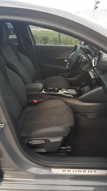 Vue intérieure côté conducteur de la Peugeot 208 Hybrid 110 e-DCS6 GT 2025 gris, sièges noirs et cockpit numérique visible.