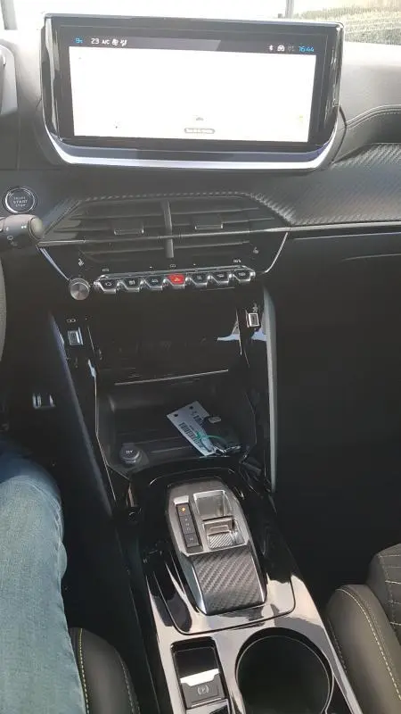 Vue intérieure centrée sur la console centrale et l'écran tactile de la Peugeot 208 Hybrid 110 e-DCS6 GT gris, avec levier de vitesse automatique.