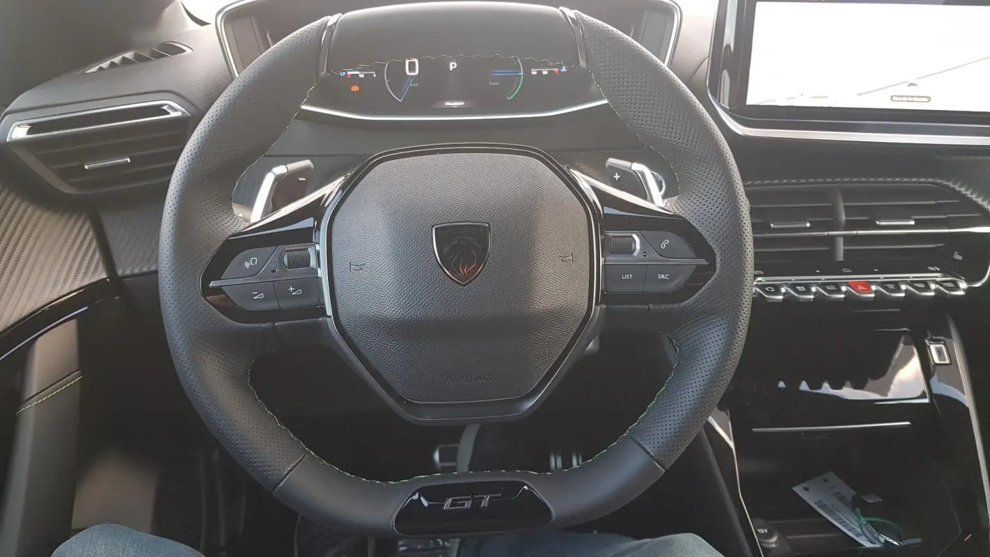 Vue intérieure centrée sur le volant GT et le cockpit numérique du Peugeot 208 Hybrid 110 e-DCS6 gris.
