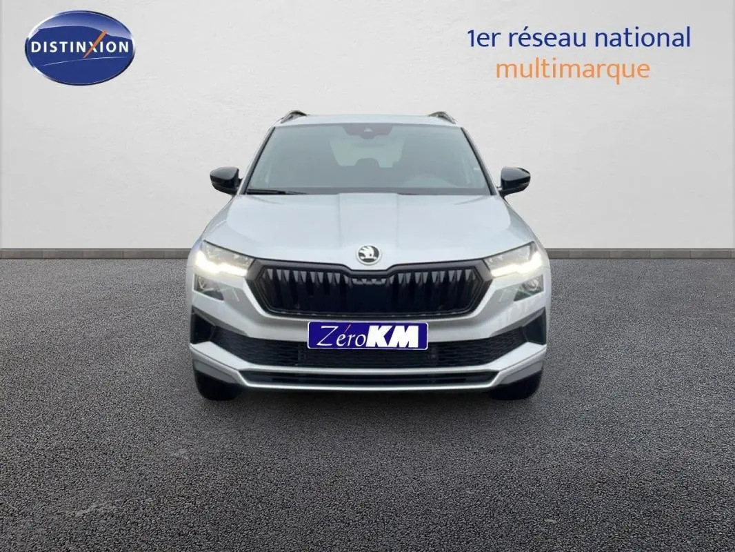 Vue frontale d'un Skoda Karoq argent 2025 avec calandre noire et phares allumés sur fond neutre.