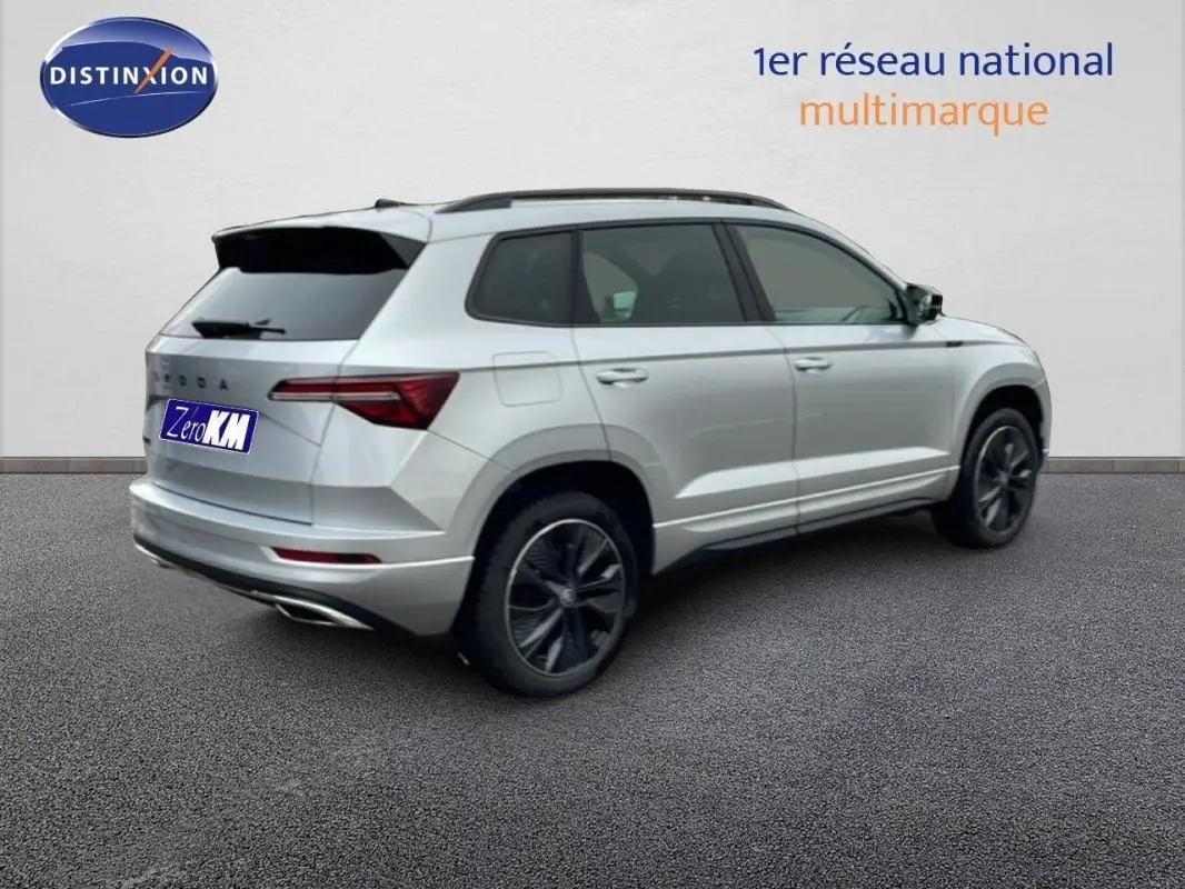 Vue 3/4 arrière droite d’un Skoda Karoq argent 2025 avec barres de toit et vitres arrière teintées.